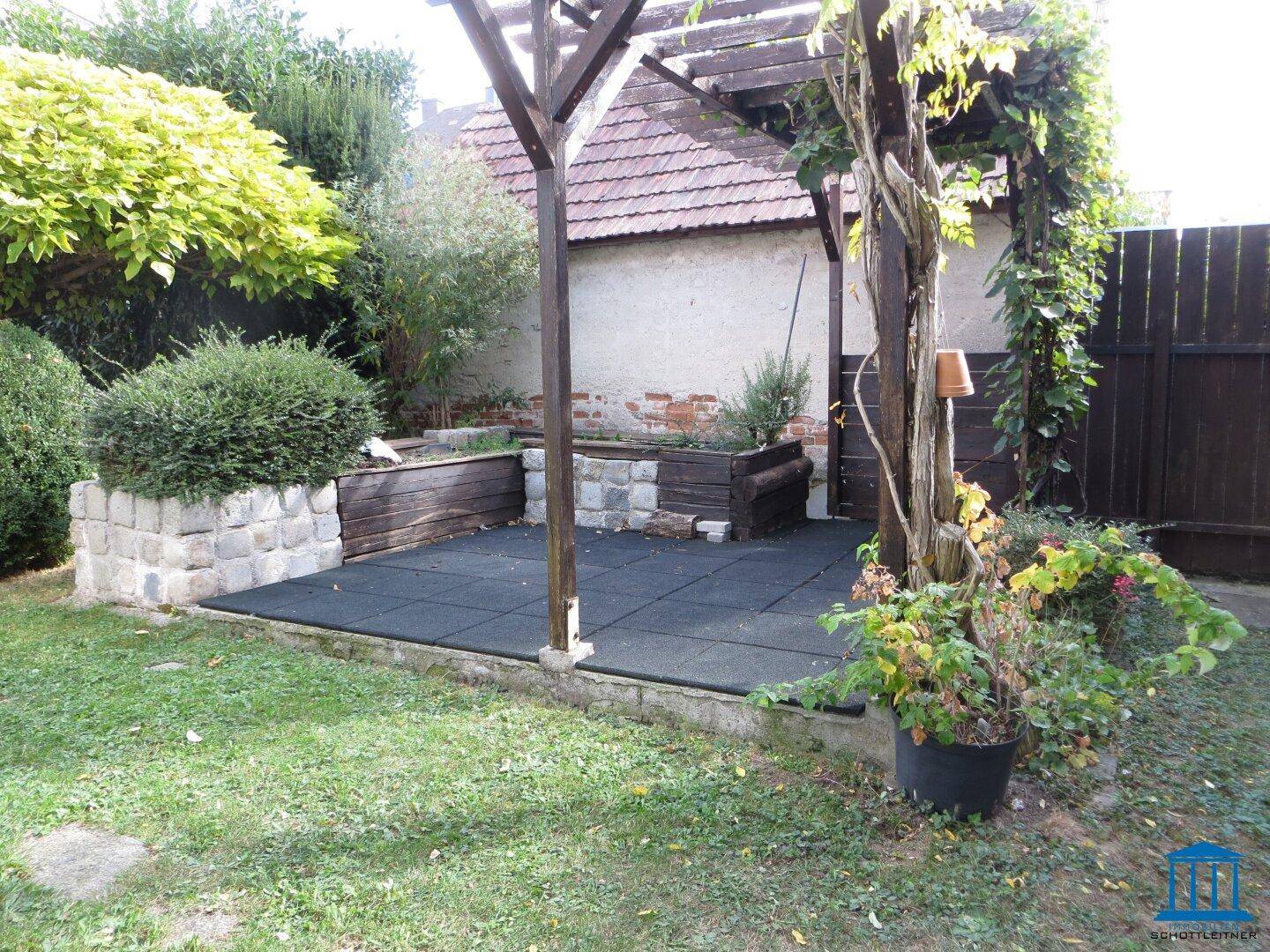 Gemütlicher Terrassenbereich mit Pergola und Sitzgelegenheiten, umgeben von Grünflächen.