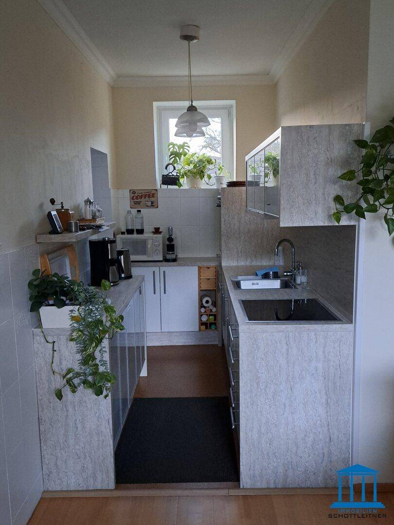 Schmale Küche mit Einbauschränken, Spüle und Fenster, das viel Licht spendet.