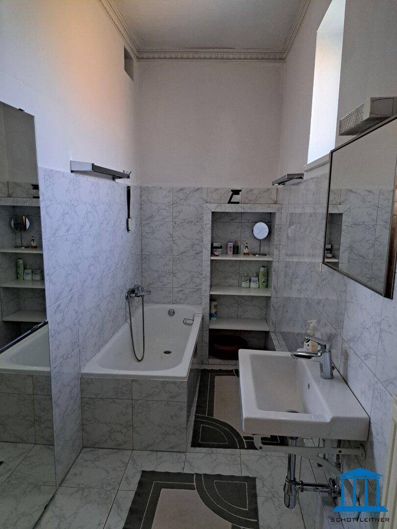 Badezimmer mit Badewanne, Waschbecken und hellen Marmorfliesen an Wänden und Boden.