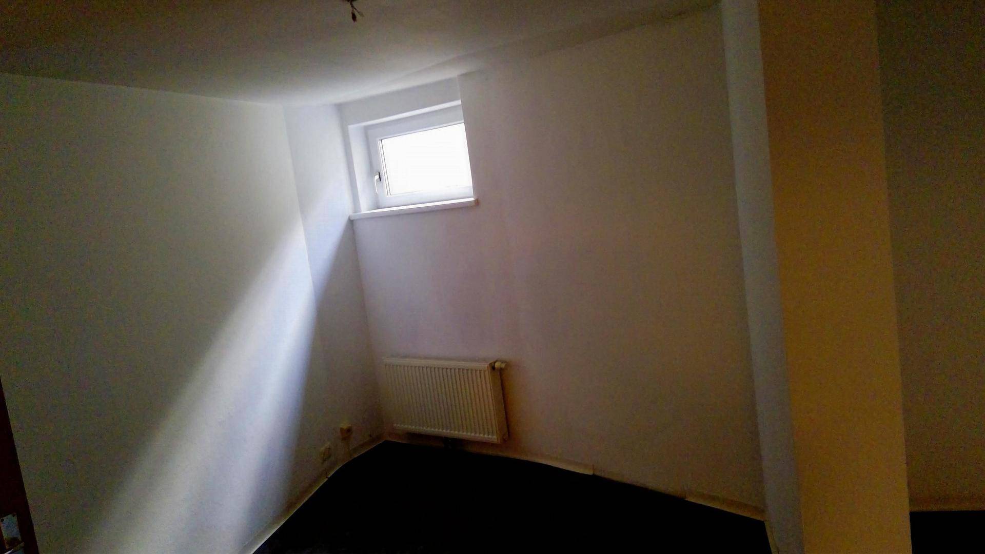 Kleiner Raum mit Fenster, Heizkörper und dunklem Laminatboden.