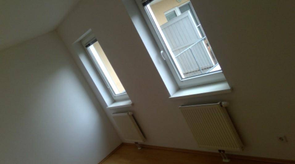 Dachgeschossraum mit schrägen Wänden, zwei Fenstern und Heizkörpern unter den Fenstern.