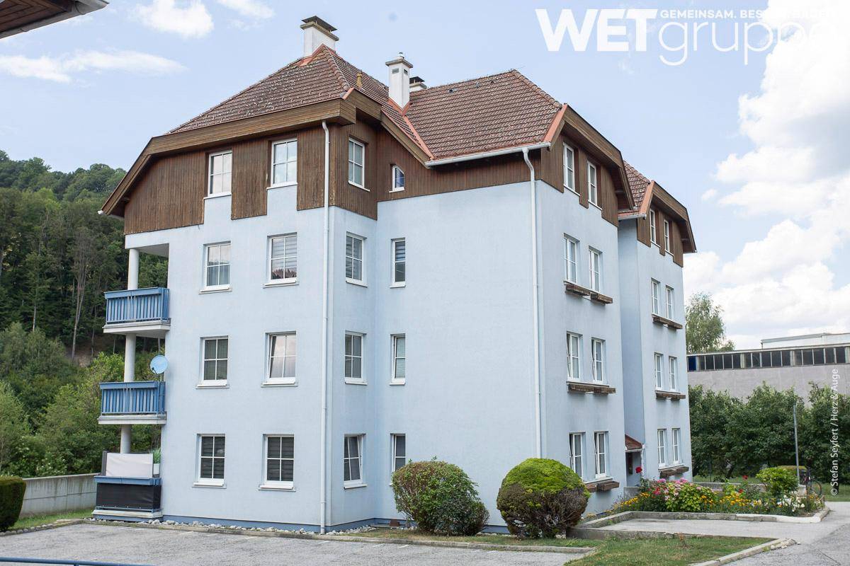 Ansicht eines Wohngebäudes mit hellblauer Fassade, Holzverkleidung und blauen Balkonen.