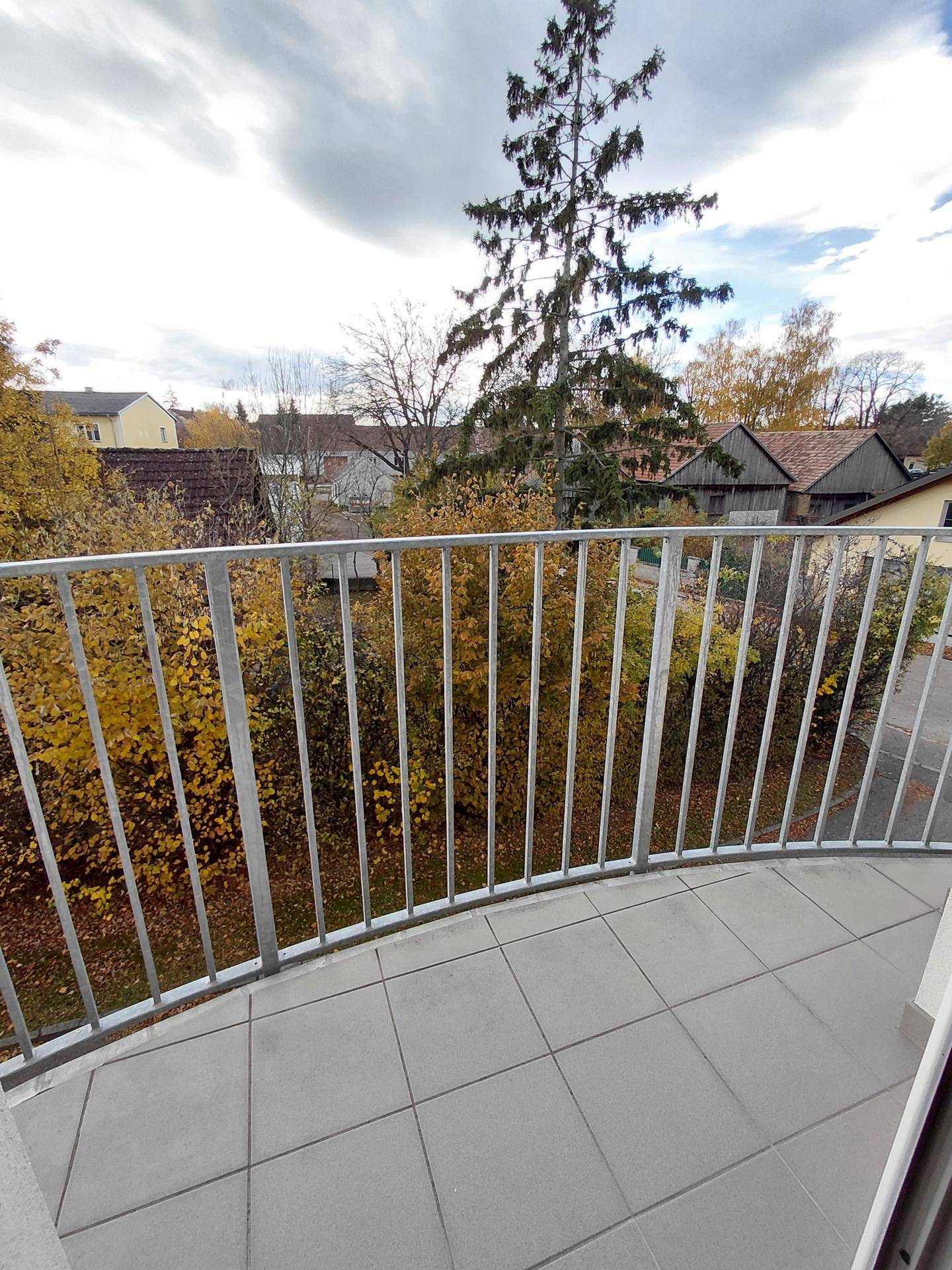 Balkon mit grauen Fliesen und Metallgeländer, bietet einen Blick auf Bäume und die Nachbarschaft.
