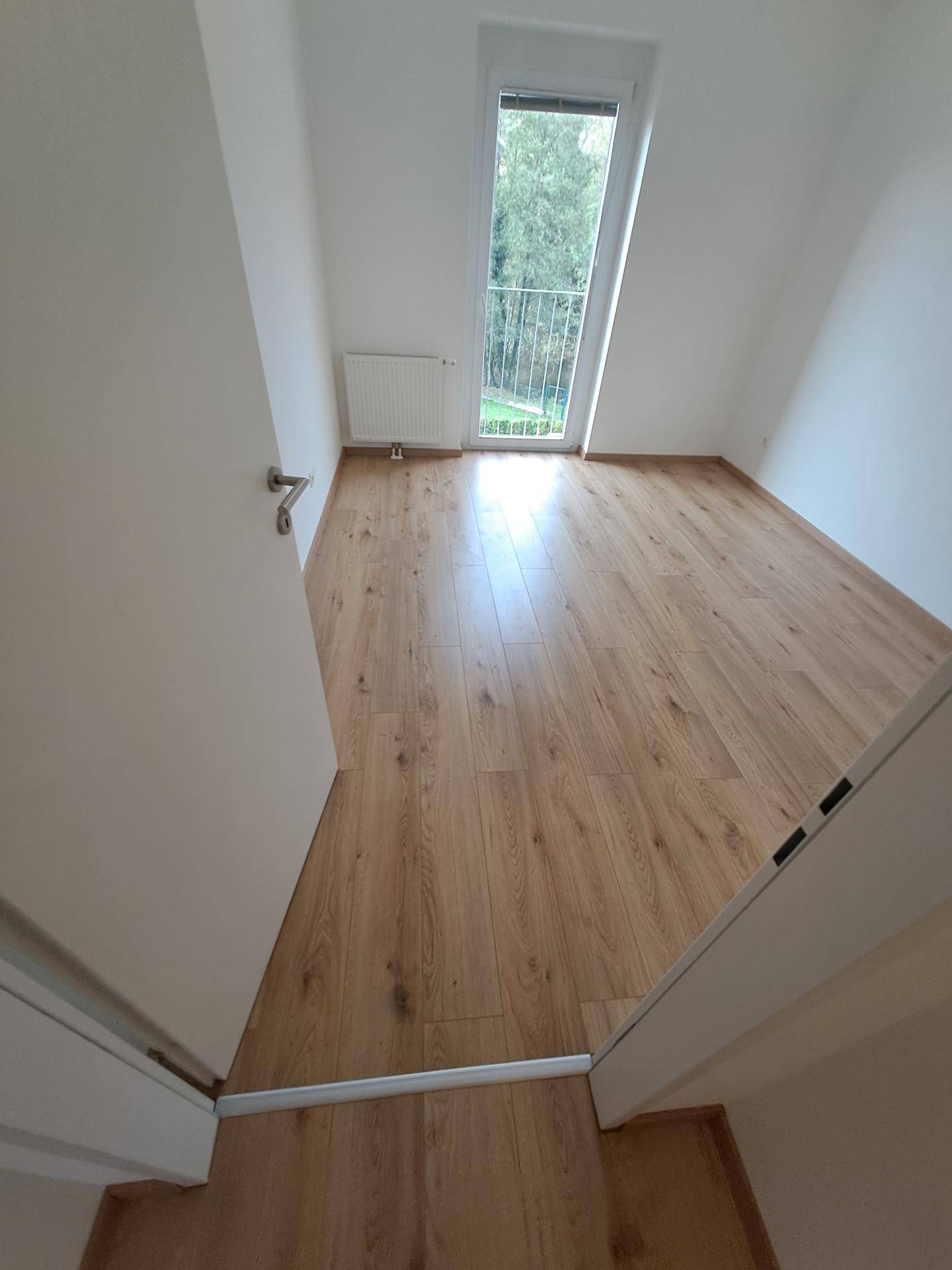 Helles Schlafzimmer mit Laminatboden und Zugang zu einem Balkon, der viel Licht bietet.