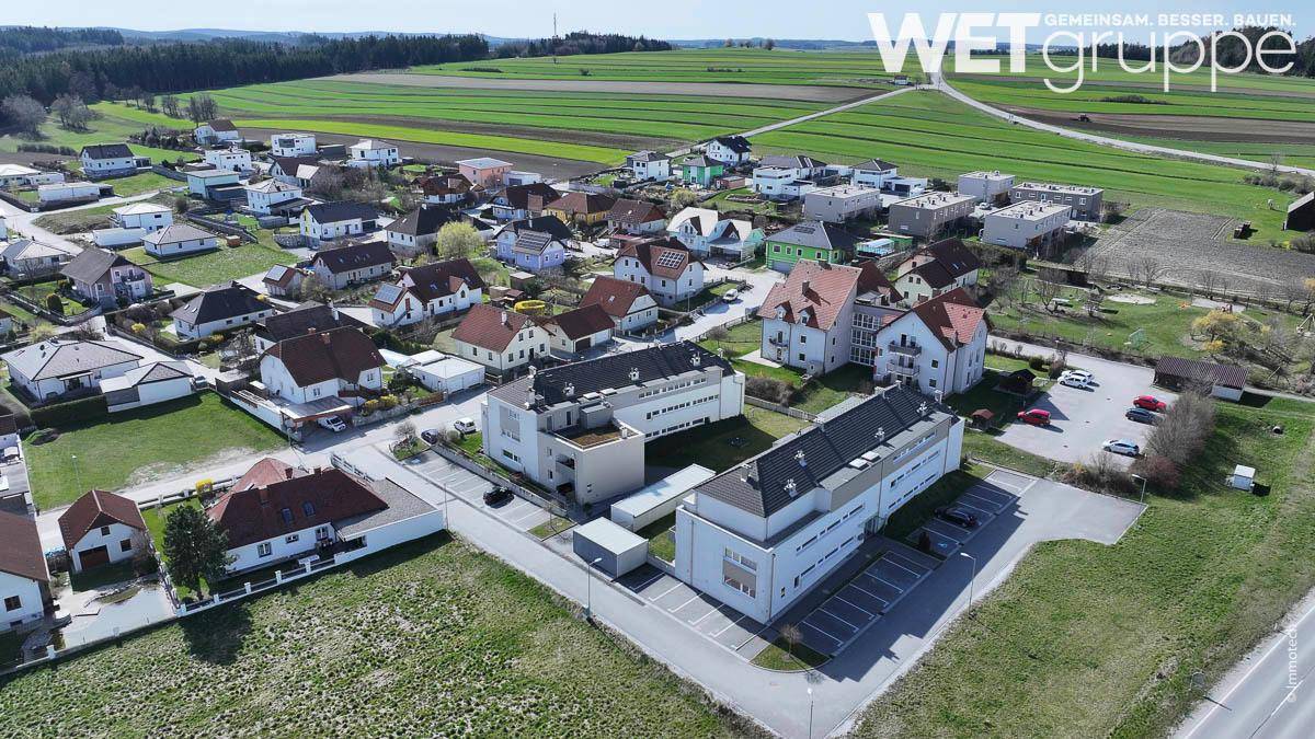 Luftaufnahme einer Wohnsiedlung mit modernen Mehrfamilienhäusern und Einfamilienhäusern, umgeben von grünen Feldern.