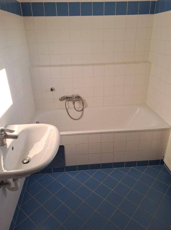 Badezimmer mit blauen und weißen Fliesen, einer Badewanne und einem Waschbecken.