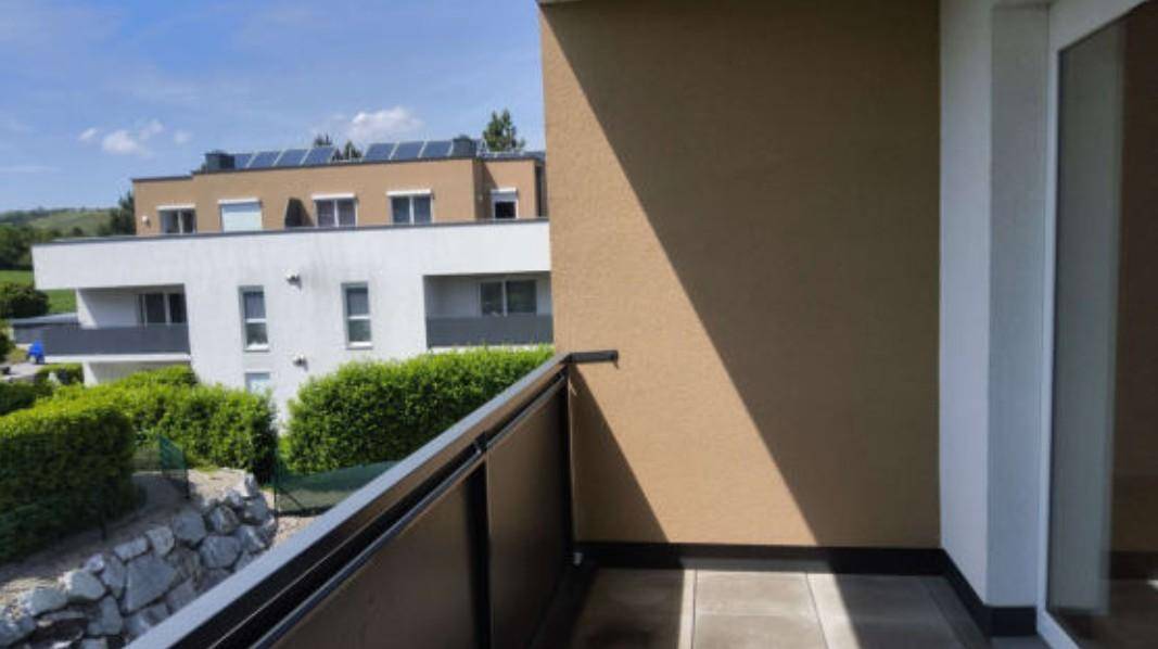 Balkon mit moderner Brüstung und Ausblick auf die umliegenden Gebäude und die grüne Landschaft.