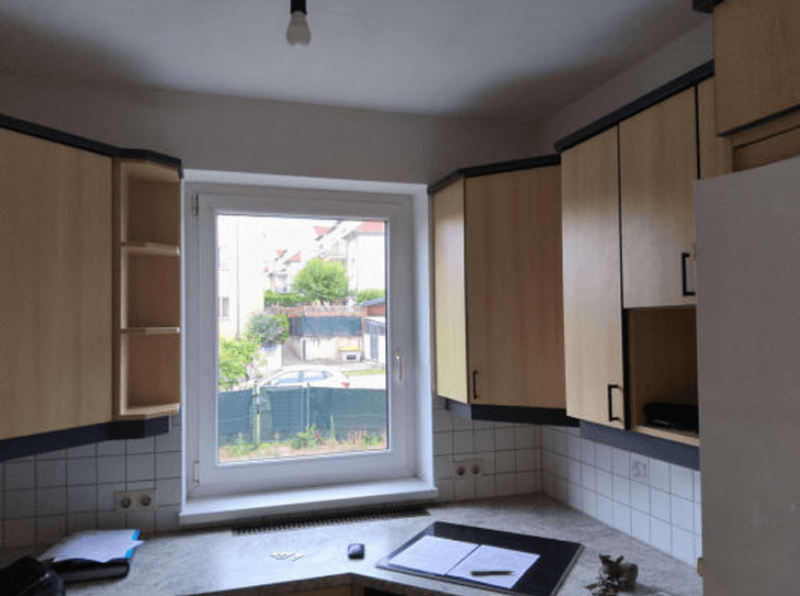 Küche mit hellen Holzschränken, Arbeitsplatte und Fenster mit Blick ins Grüne.