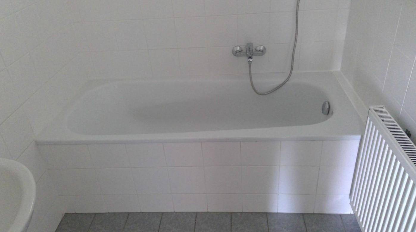 Helles Badezimmer mit weißer Badewanne und grauen Fliesen, funktional und sauber.
