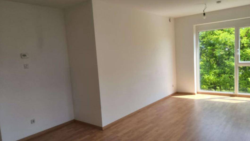 Geräumiger, heller Innenraum mit Holzboden und großen Fenstern, die viel Tageslicht hereinlassen.
