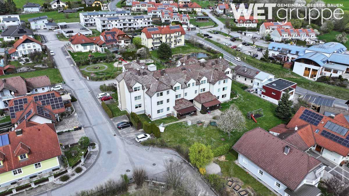 Weitläufige Luftaufnahme eines Wohnkomplexes in einer grünen Umgebung mit vielen Häusern.
