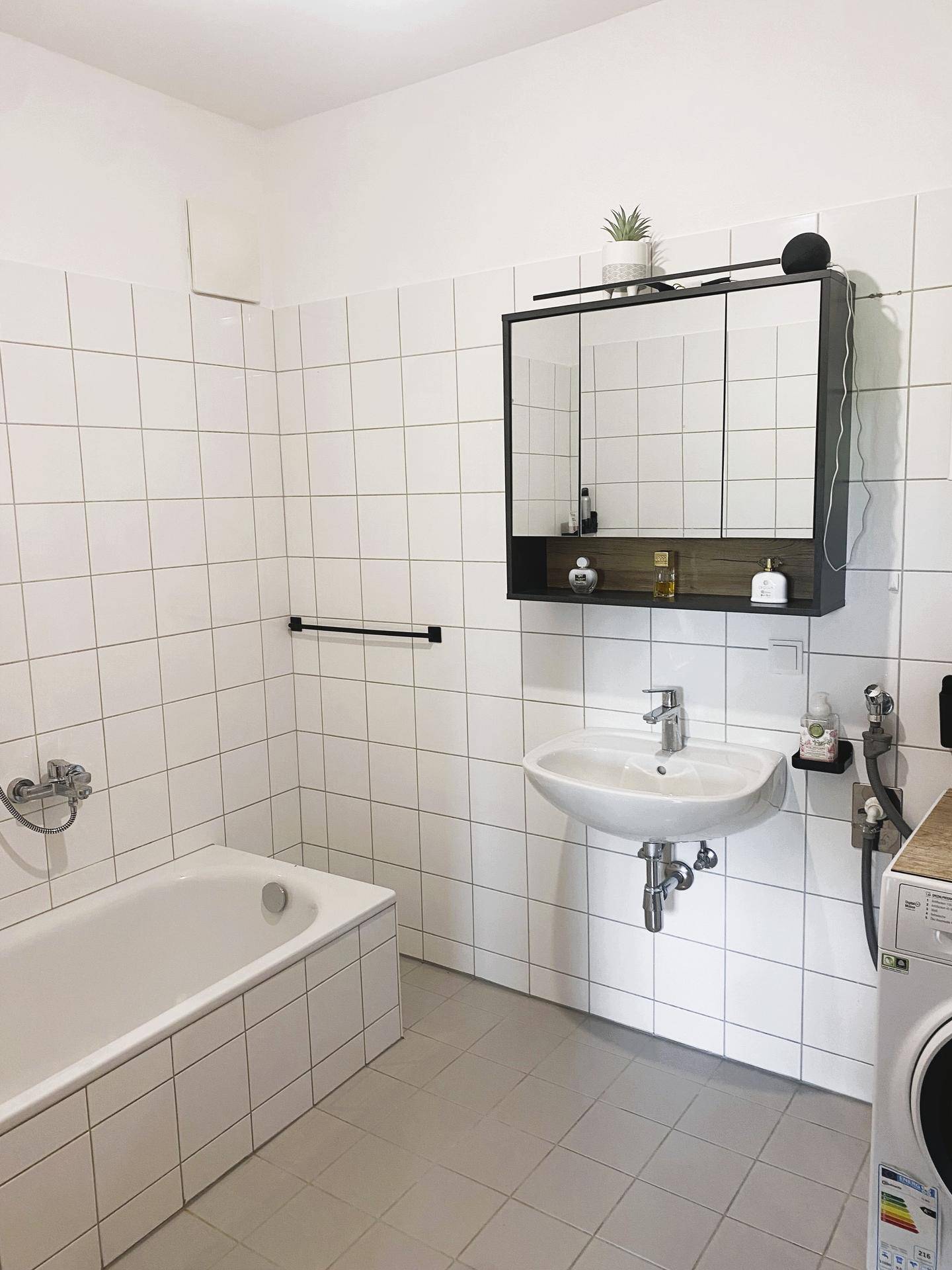 Funktionales Badezimmer mit Badewanne, Waschbecken, Spiegelschrank und Waschmaschine.