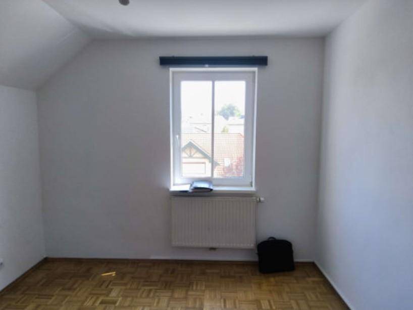 Helles Zimmer mit Parkettboden und Fenster mit Blick auf die Nachbarschaft.