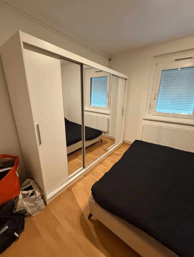 Schlafzimmer mit großem Spiegelschrank, Doppelbett und hellem Laminatboden, funktional eingerichtet.