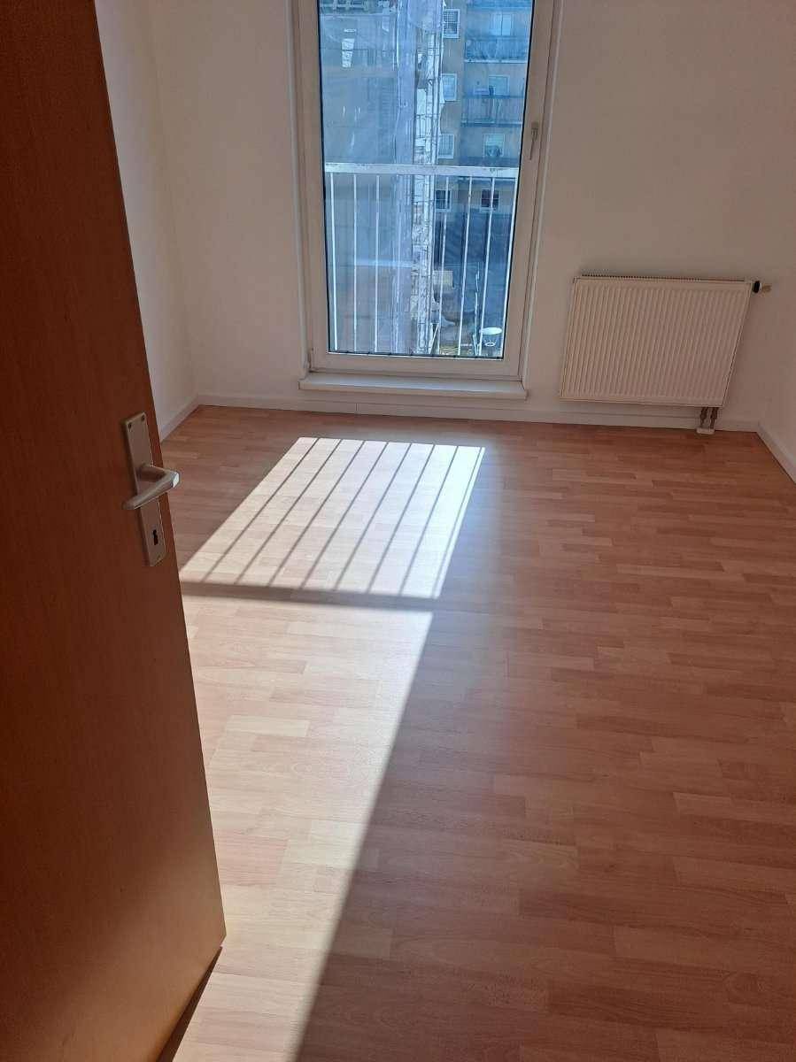 Helles Zimmer mit Laminatboden, Heizkörper und Zugang zu einem französischen Balkon.
