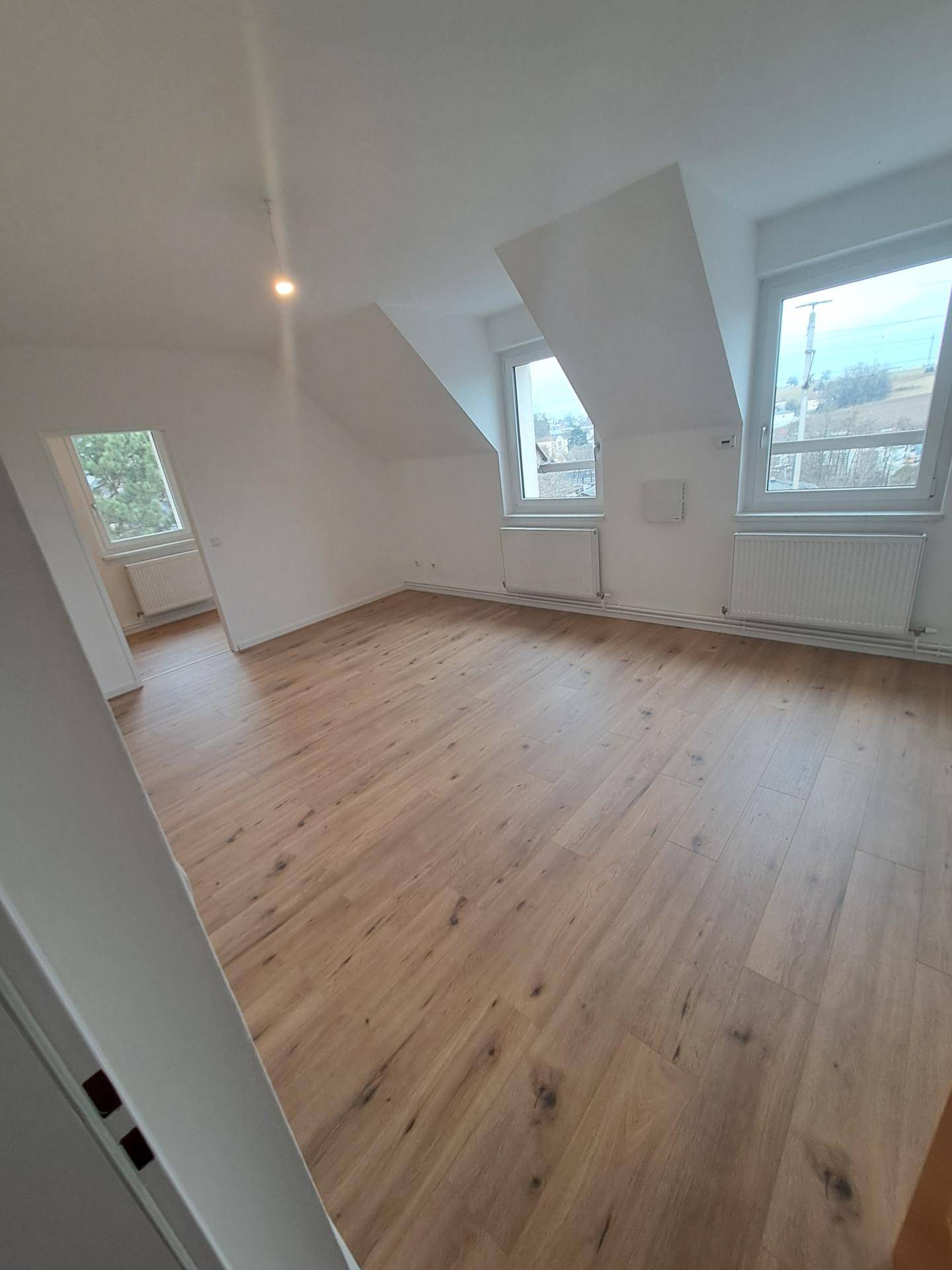 Geräumiger Wohnbereich im Dachgeschoss mit Holzboden und mehreren Fenstern für viel Tageslicht.