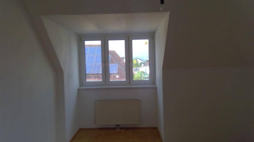 Heller Raum mit Fenster und Blick auf ein Dach mit Solaranlage, ausgestattet mit Heizkörper.