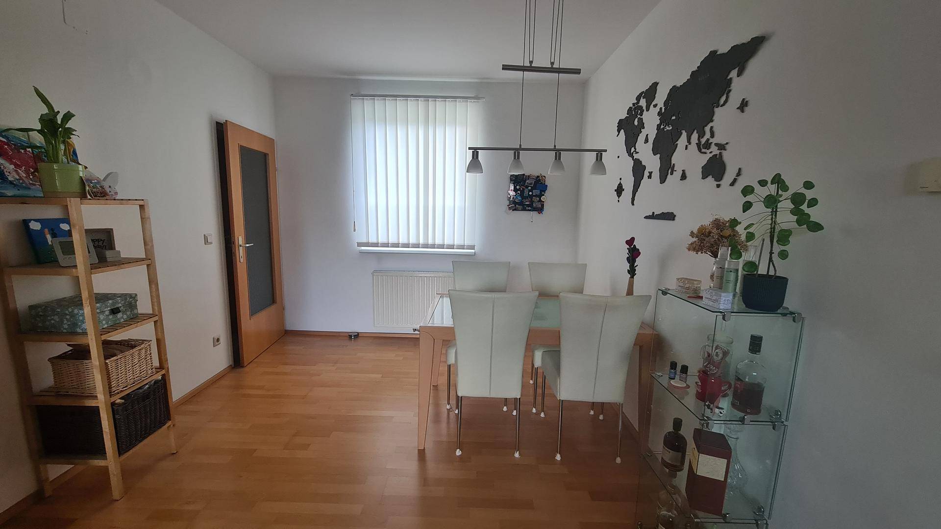 Essbereich mit Holztisch, weißen Stühlen, Regal und einer Weltkarte als Wanddekoration.