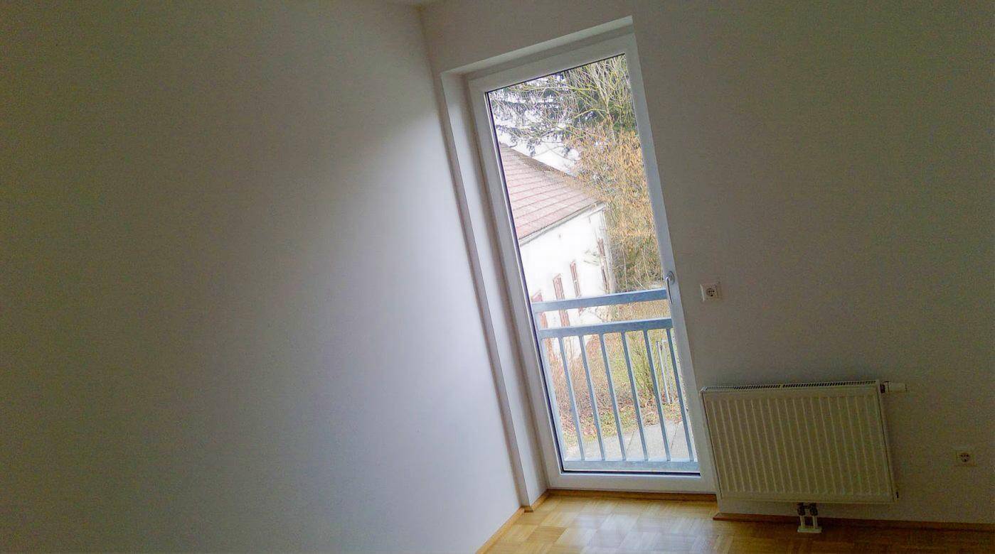 Heller Raum mit Holzboden und einem Fenster, das einen Blick nach draußen bietet.