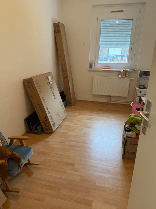 Helles Zimmer mit Laminatboden und Fenster mit Rollladen, derzeit als Abstellraum genutzt.
