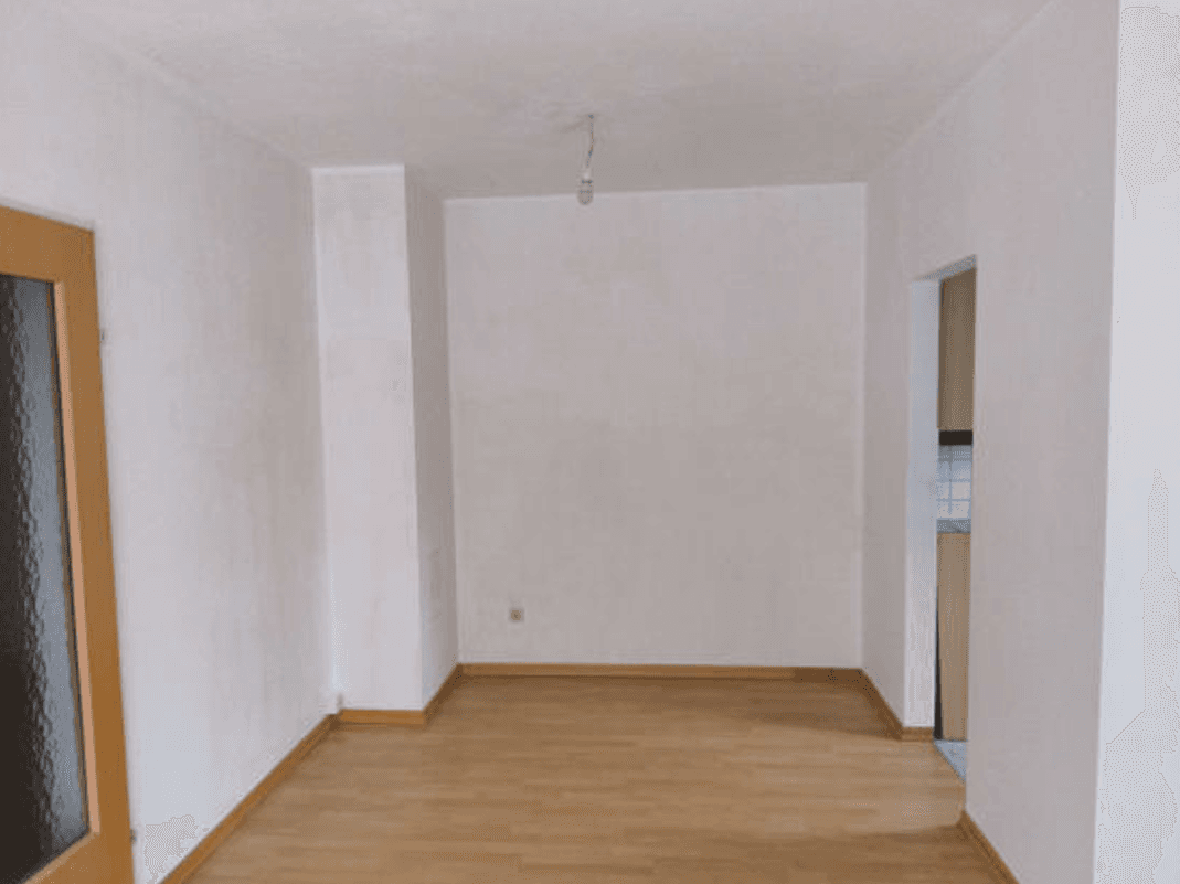 Heller, leerer Raum mit Holzfußboden und einer Tür mit Glaseinsatz.