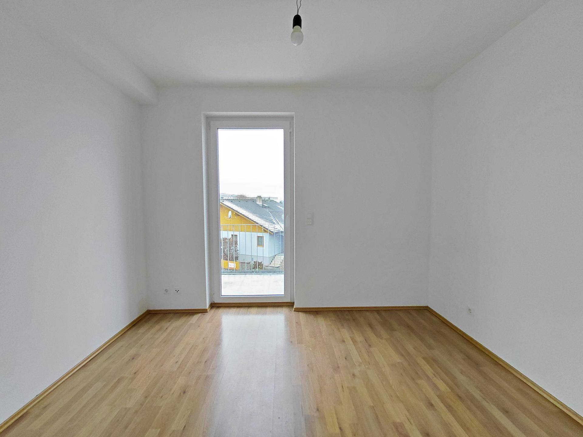 Helles Schlafzimmer mit Laminatboden und Balkontür, bereit zur Einrichtung, in gutem Zustand.
