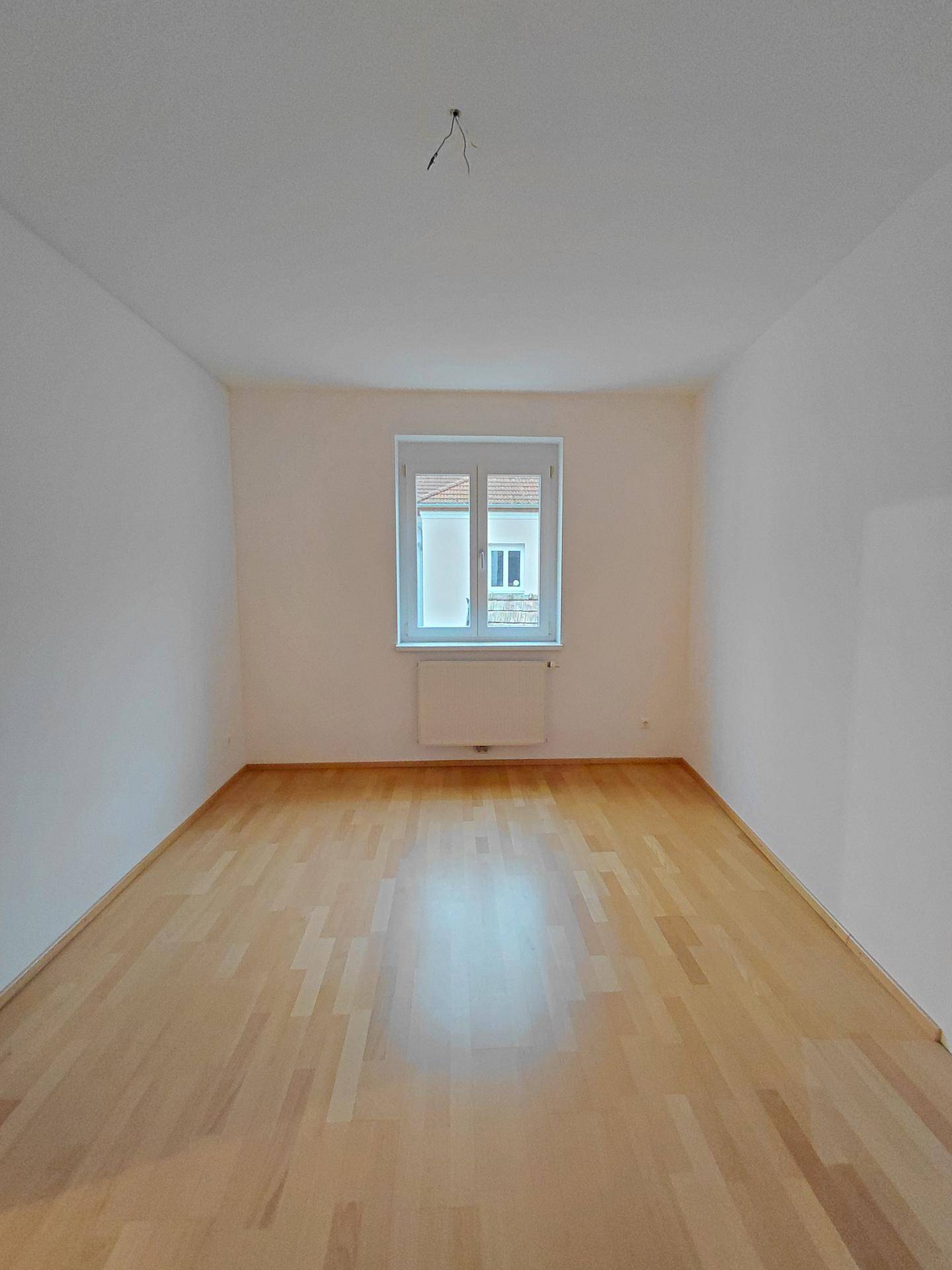 Helles Schlafzimmer mit Parkettboden und einem Fenster, bereit zur individuellen Gestaltung.