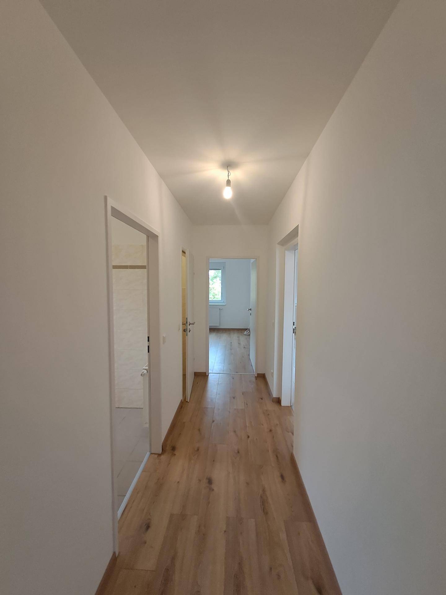 Heller Flur mit Laminatboden und weißen Wänden, der zu verschiedenen Räumen der Wohnung führt.