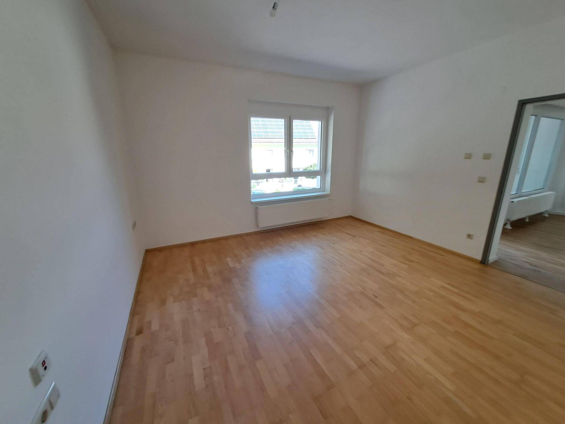 Helles Schlafzimmer mit Holzparkettboden und einem großen Fenster, das viel Licht hereinlässt.