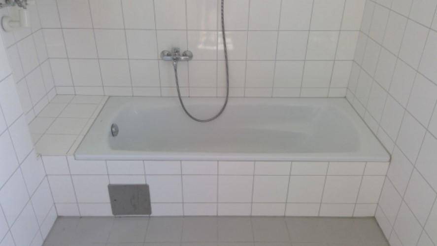 Badezimmer mit weiß gefliester Badewanne und Duschvorrichtung in gutem Zustand.