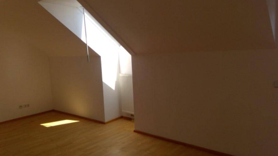 Lichtdurchfluteter Dachgeschossraum mit Holzboden, schrägen Wänden und großem Dachfenster.