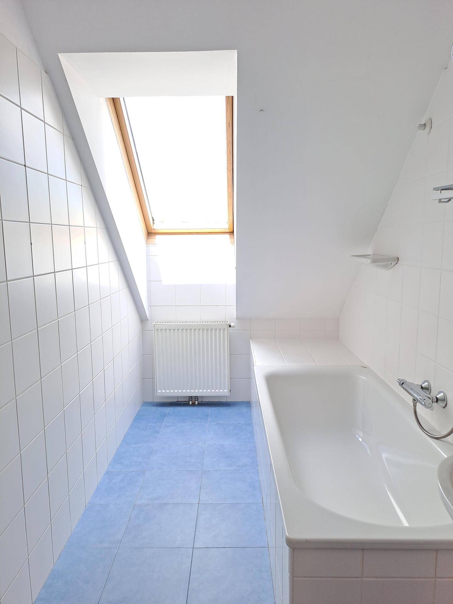 Badezimmer im Dachgeschoss mit Badewanne, blauen Fliesen und Dachfenster für natürliches Licht.