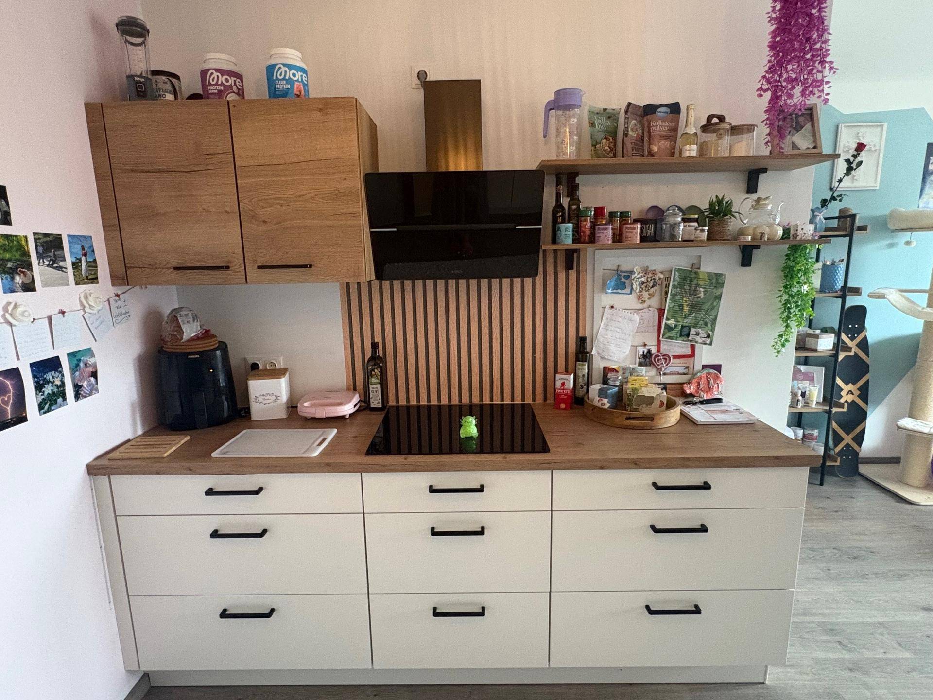 Funktionale Küche mit Holz- und weißen Schränken, Induktionskochfeld und Dunstabzugshaube.