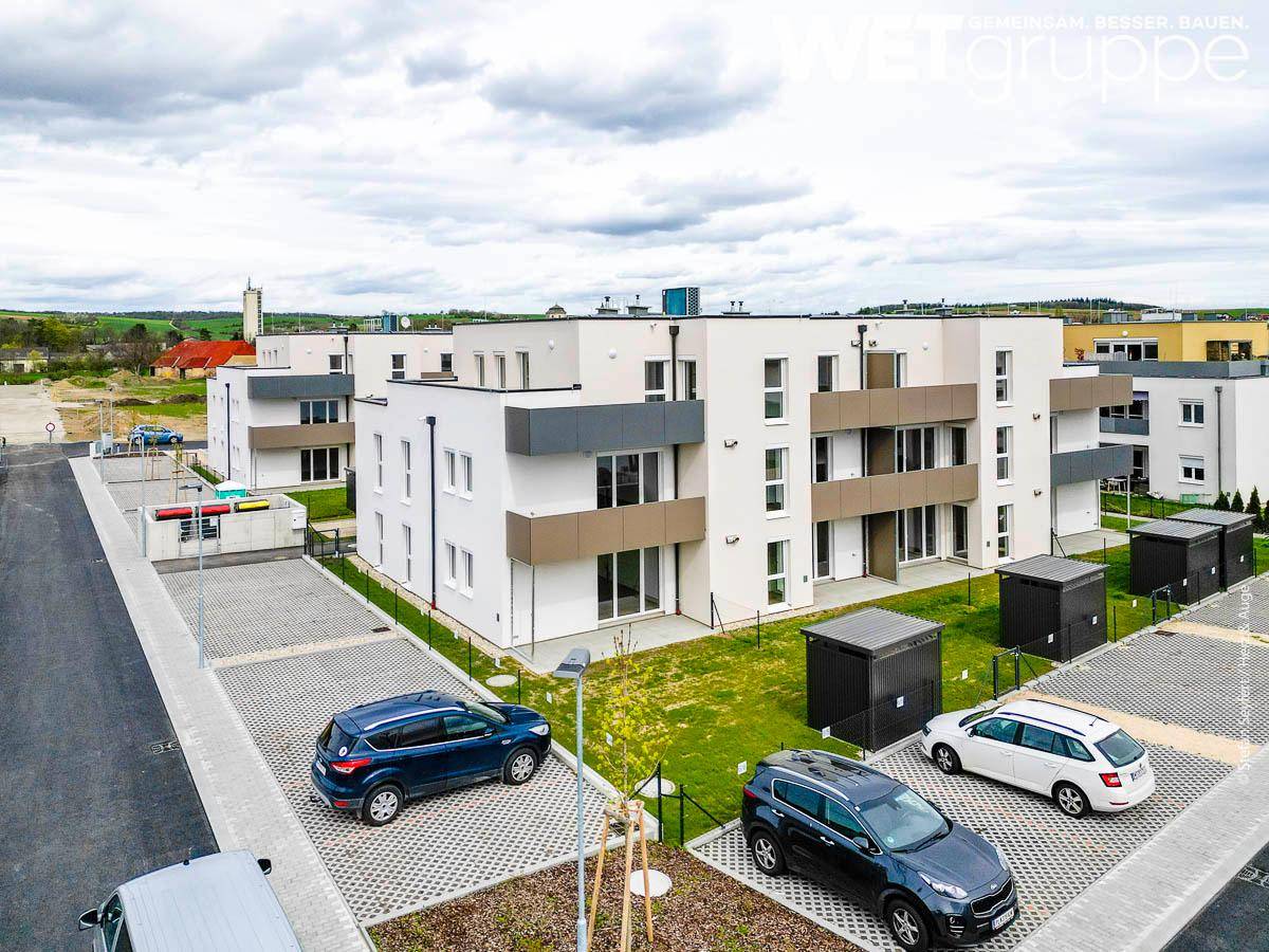 Moderne Wohnanlage mit mehreren Gebäuden, Parkplätzen und Grünflächen unter bewölktem Himmel.
