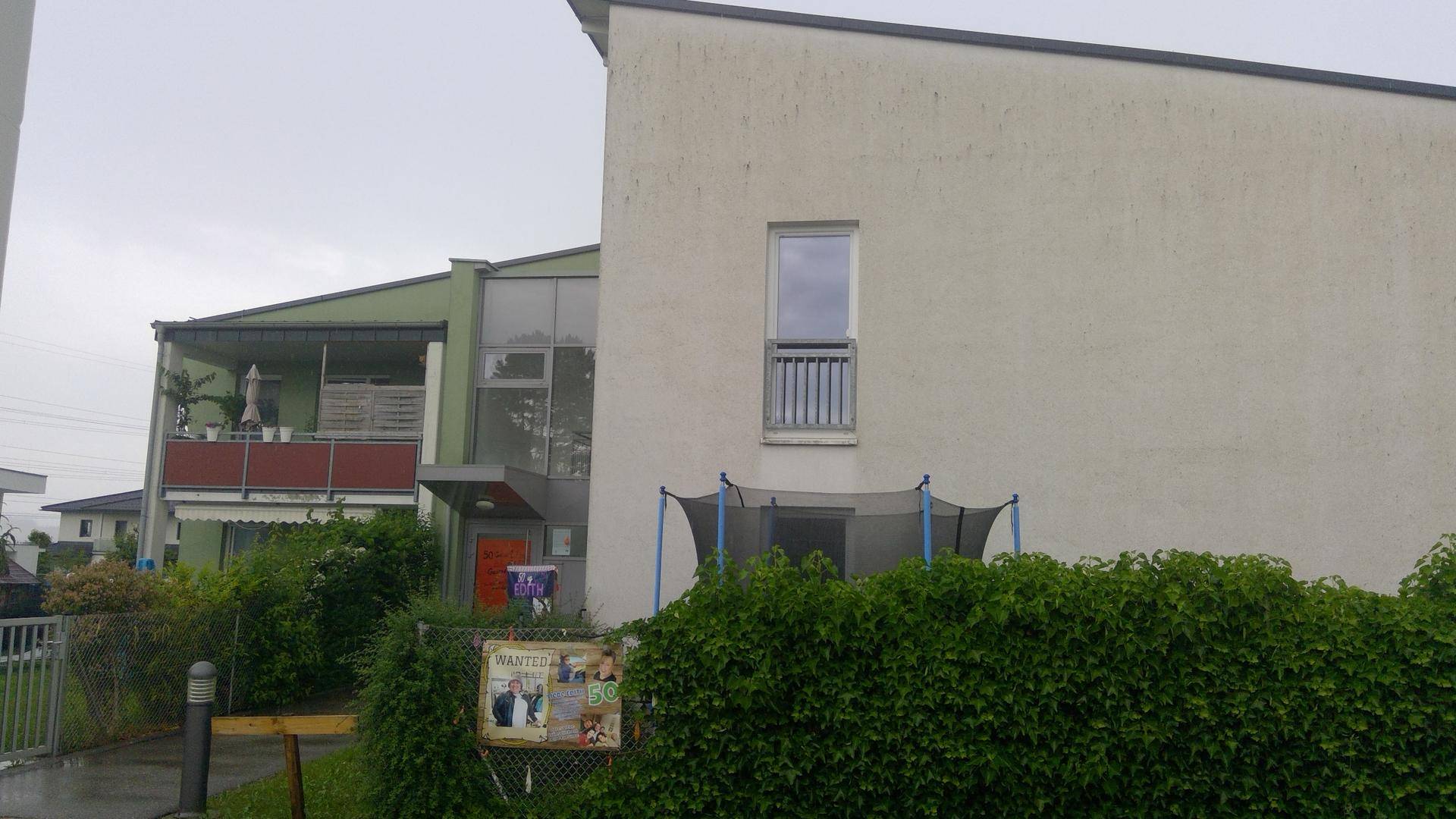Außenansicht eines modernen Gebäudes mit Balkonen und einem Trampolin im Vorgarten.