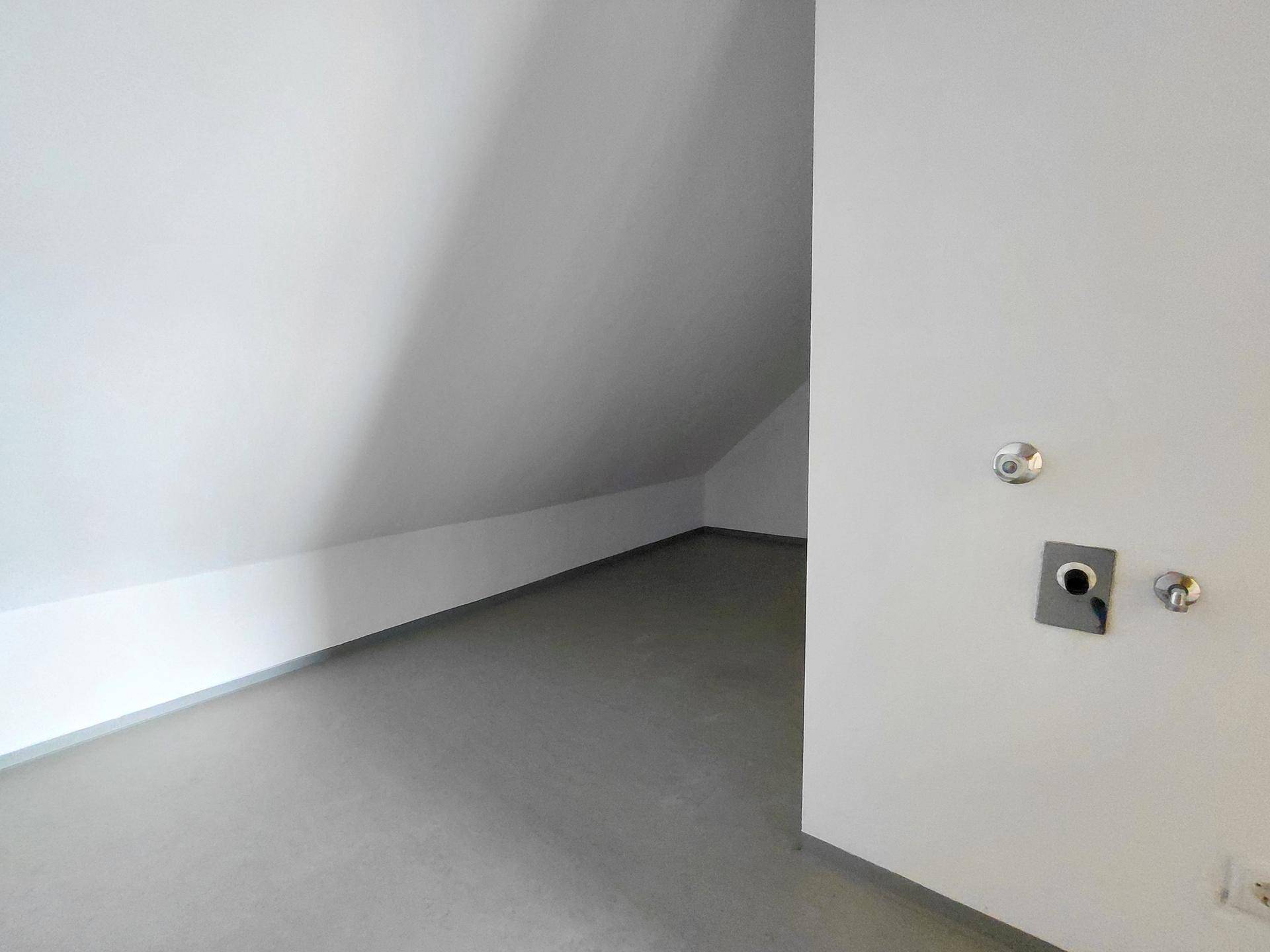 Funktionaler Raum im Dachgeschoss mit schräger Decke, grauem Boden und Anschlüssen für Geräte.
