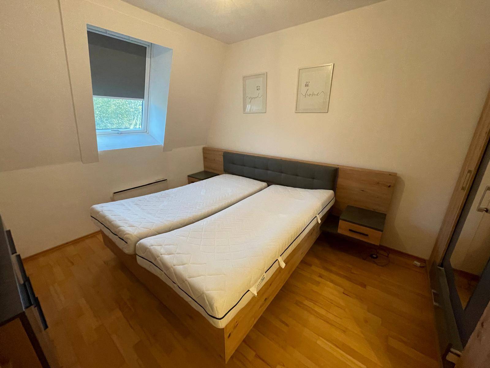 Schlafzimmer mit zwei Einzelbetten, Holzboden und Fenster mit Rollladen.