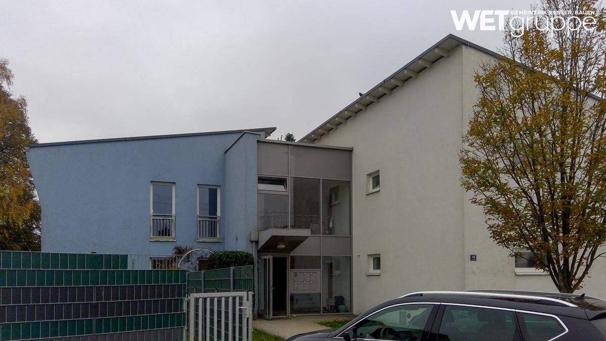 Modernes Wohngebäude mit blauer und weißer Fassade, umgeben von Bäumen und einem Zaun.