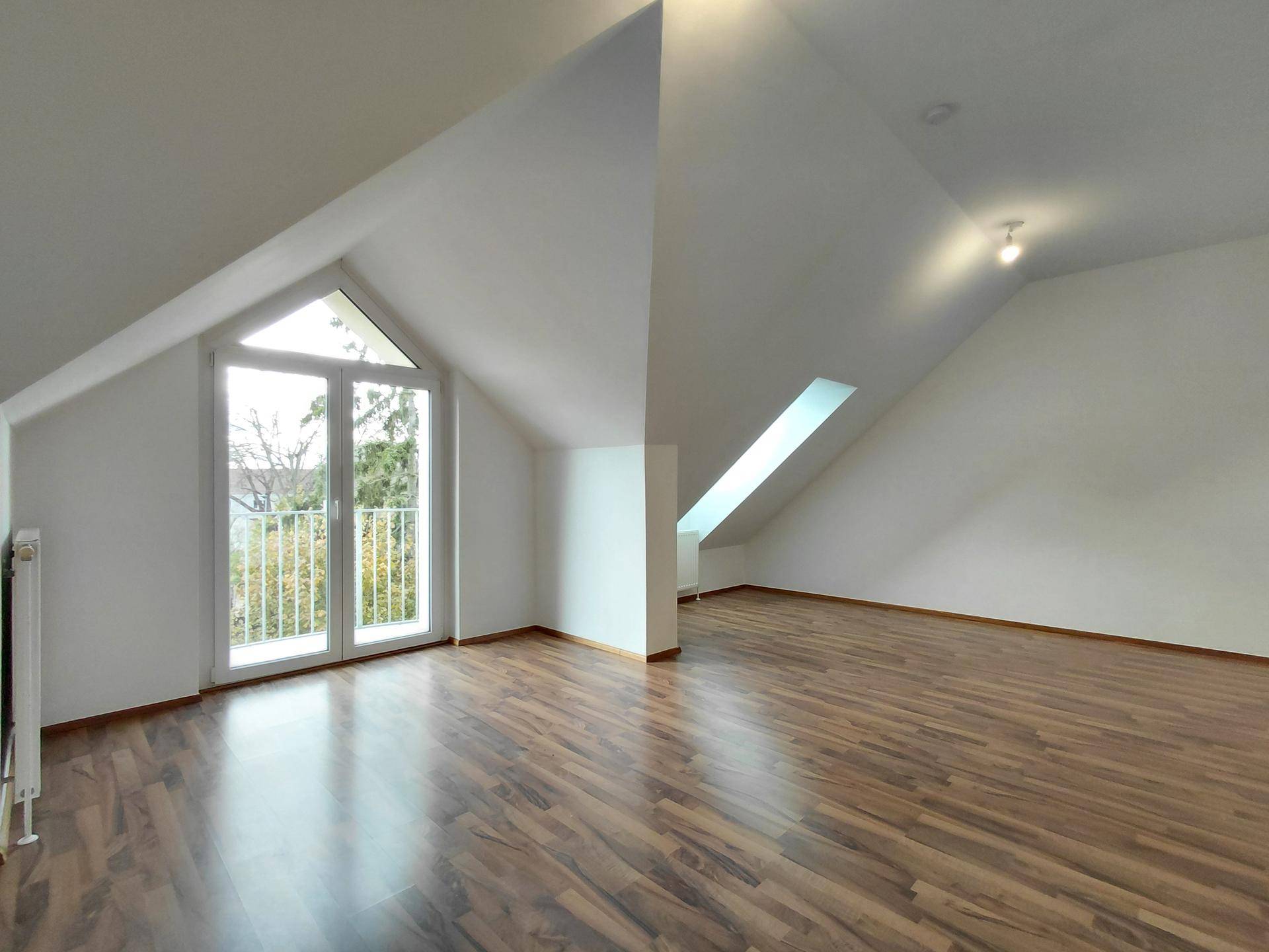 Geräumiger Wohnbereich im Dachgeschoss mit Schrägdecke, Balkonzugang und einem Dachfenster.