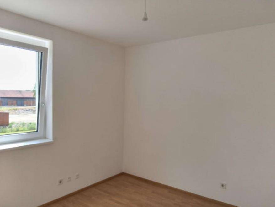 Schlichter Innenraum mit hellem Holzboden und einem Fenster, das den Raum mit natürlichem Licht versorgt.