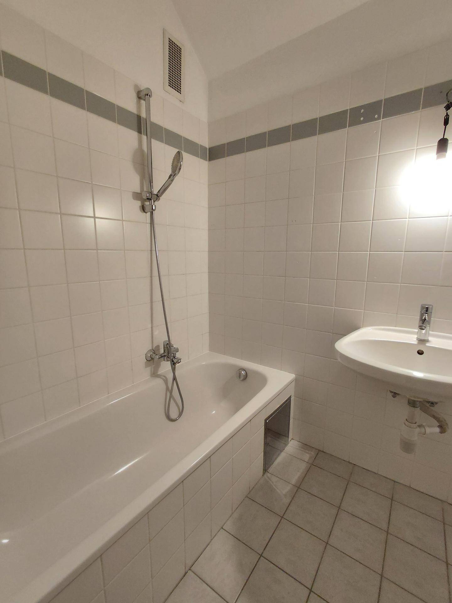 Badezimmer mit weißen Fliesen, Badewanne mit Duscharmatur und einem Waschbecken.