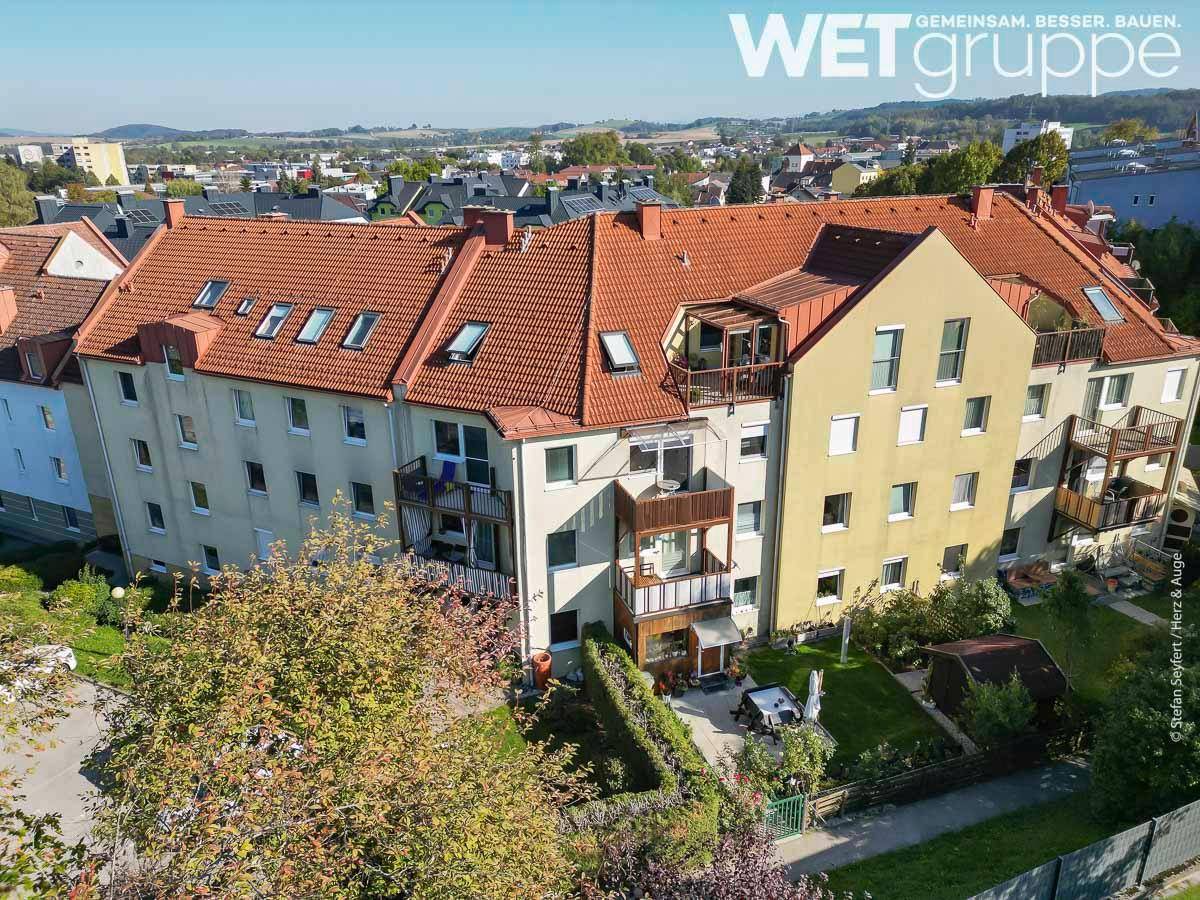 Ansicht eines Wohnhauses mit mehreren Balkonen und kleinen Gärten im Vordergrund unter blauem Himmel.