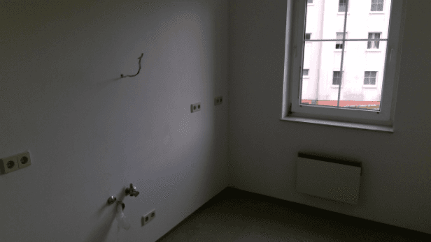 Leerer Raum mit Fenster, Heizkörper und vorbereiteten Anschlüssen für eine Küche oder Hauswirtschaftsraum.