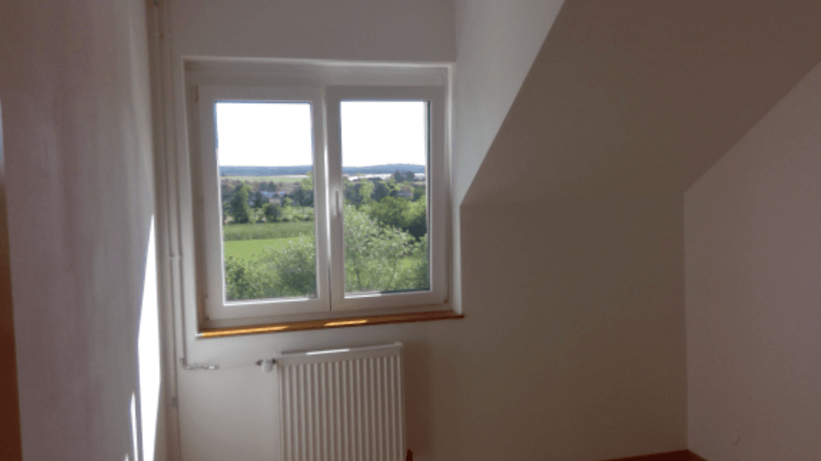 Heller Raum im Dachgeschoss mit weitem Blick ins Grüne durch das Fenster und Schrägdecken.