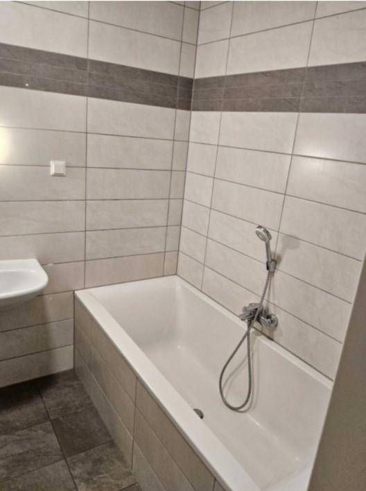 Badezimmer mit Badewanne, weißen und grauen Fliesen sowie einem Waschbecken.