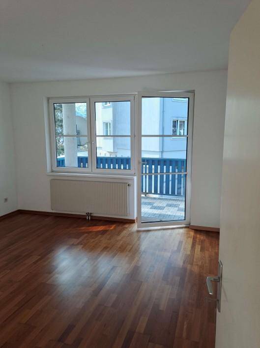 Heller Raum mit Parkettboden, weißen Wänden und direktem Zugang zu einem Balkon.