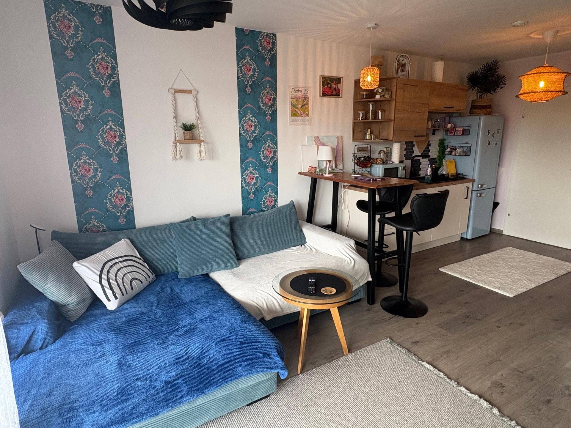 Gemütlicher Wohnbereich mit blauem Sofa, Esstisch und offener Küche im Hintergrund.