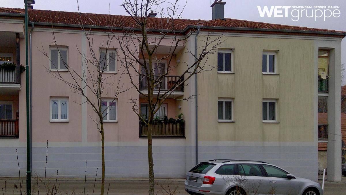 Mehrfamilienhaus mit farbiger Fassade und Balkonen, umgeben von kahlen Bäumen im Winter.