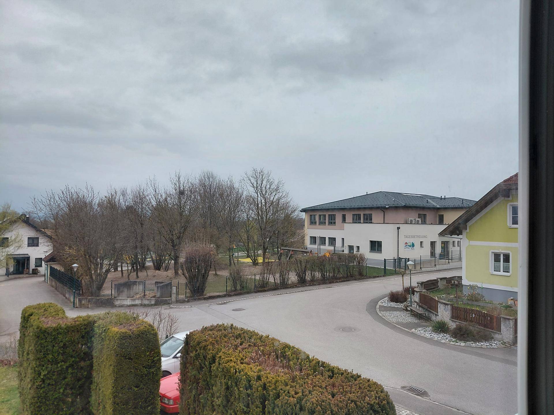 Blick aus dem Fenster auf eine ruhige Wohnstraße mit Bäumen und umliegenden Gebäuden.