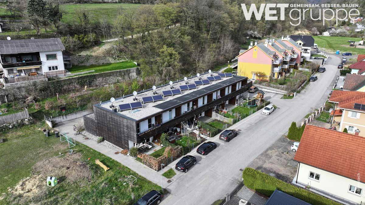Luftaufnahme einer modernen Reihenhausanlage mit Photovoltaikanlage auf dem Dach und Gärten.